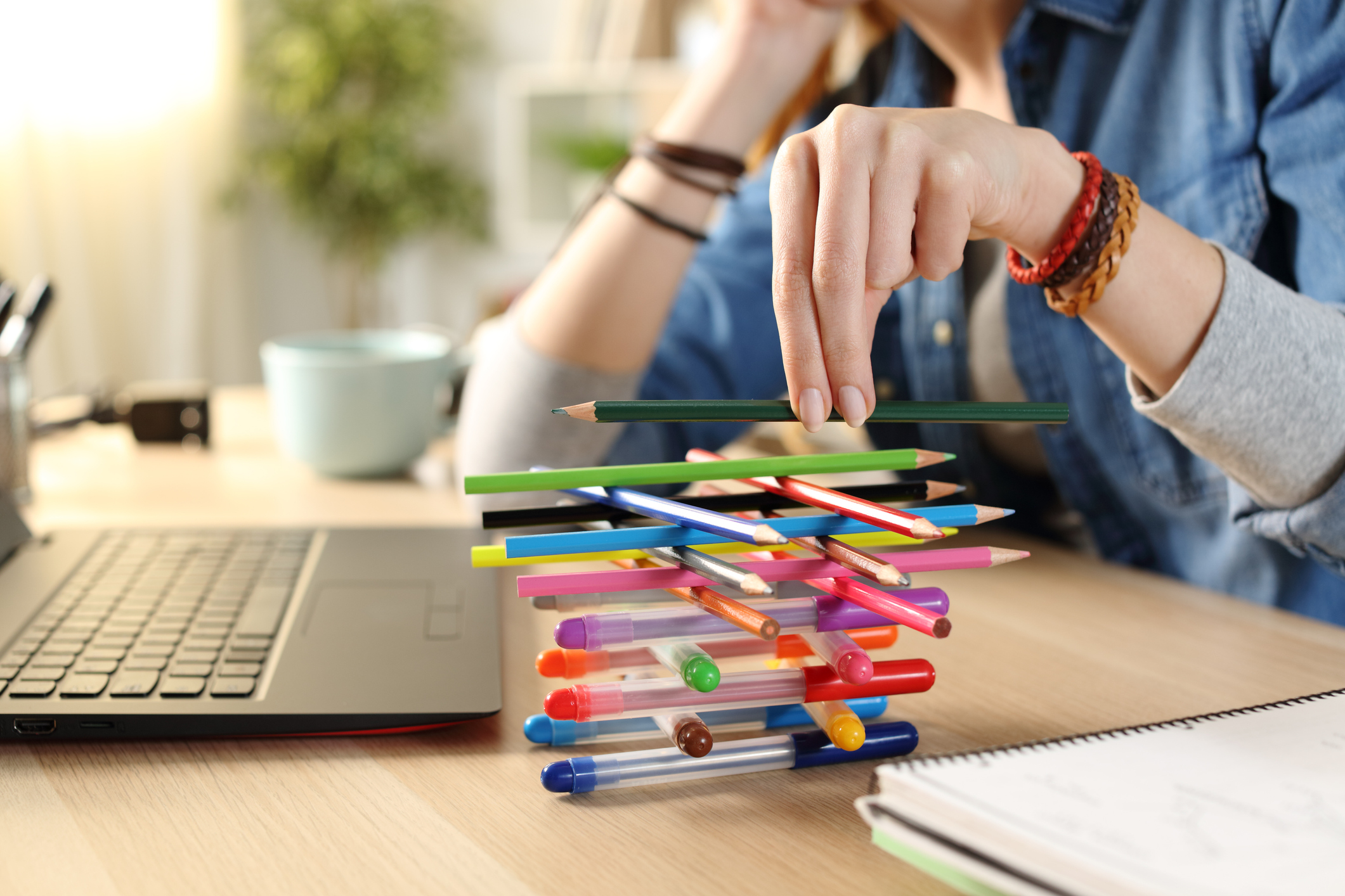 A woman sitting at a desk in front of a laptop stacking pens while distracted from BCBA Exam Prep