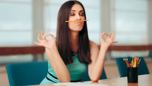 Woman "meditating" at a desk while holding a pencil between her lips and nose
