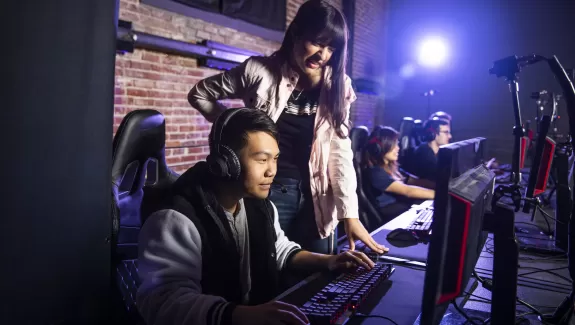 a female esports coach watching and helping a male gamer